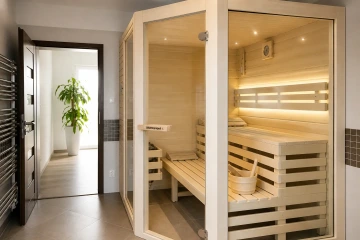 Moderní interiérová sauna z osiky s prosklenou stěnou, LED osvětlením a lavicemi ve světlém minimalistickém prostoru Saunaproject
