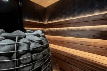 Detail saunových kamen s kameny, dřevěným obložením, kamennou stěnou a nepřímým osvětlením.